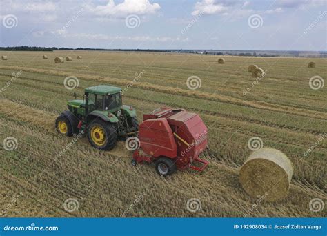 A Tractor Uses A Trailed Bale Machine To Collect Straw In The Field And