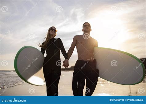 Romantic Young Couple Walking With Surfboards On Sunset Beach And