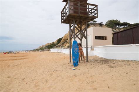 Atractiva Mujer Madura Con Gafas De Sol De Pelo Rizado Y Bikini Agarrando Una Tabla De Surf Azul