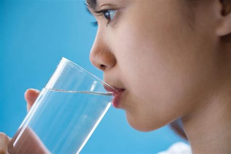 Primer Plano De Una Mujer Bebiendo Agua De Un Vaso Contra Un Fondo Azul