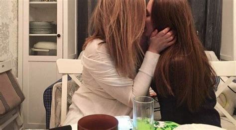 Two Women Sitting At A Table Kissing Each Other