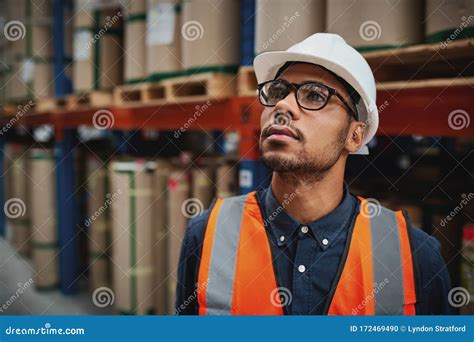 Warehouse Male Supervisor In Uniform And Helmet Thinking Standing In