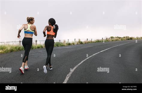 Rear View Of Two Women Athletes Running On Road Early On A Foggy