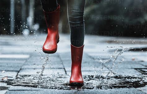 Girl Wearing Rubber Boots Splashing Water While Jumping In Puddle On