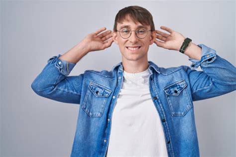 Caucasian Blond Man Standing Wearing Glasses Smiling Pulling Ears With