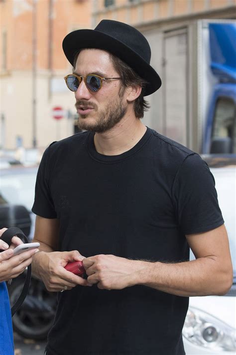 A Man In A Black Hat Is Looking At His Cell Phone And Holding An Apple