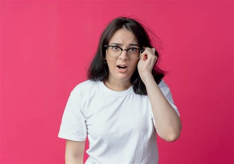 Impresionada joven bastante caucásica vistiendo y agarrando gafas