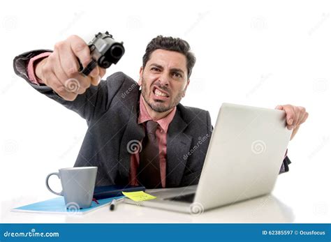 Businessman At Office Desk Working On Computer Laptop Pointing Gun