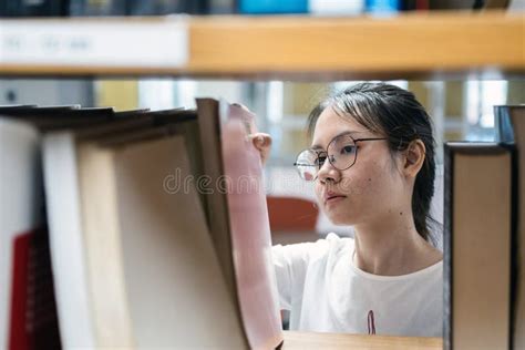 An Asian Girl Is Looking At Books On A Shelf In Library Stock Photo