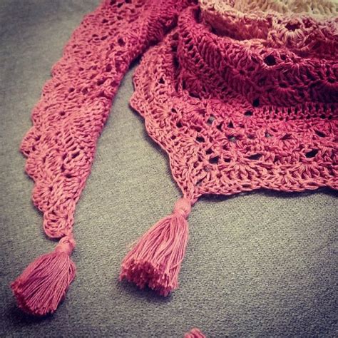 A Pink Crocheted Scarf With Tassels Laying On Top Of A Bed