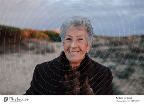 Positive Senior Woman Smiling While Resting On Sandy Seashore In