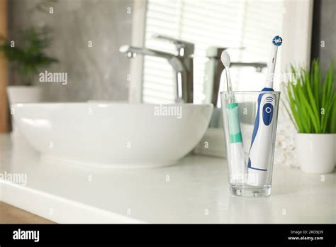 Electric Toothbrushes In Glass Near Vessel Sink On Bathroom Vanity