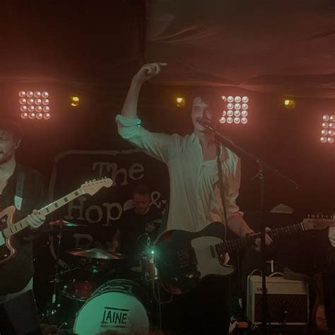 three men on stage singing and playing guitar with one holding his arm ...