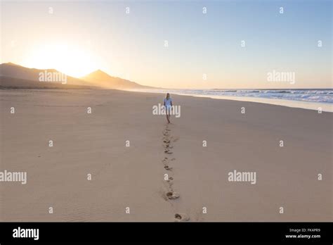 Lady Walking On Sandy Beach In Sunset Leaving Footprints Behind Stock