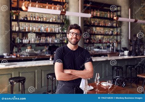 Portrait Of Male Waiter Standing In Bar Restaurant Before Service Stock