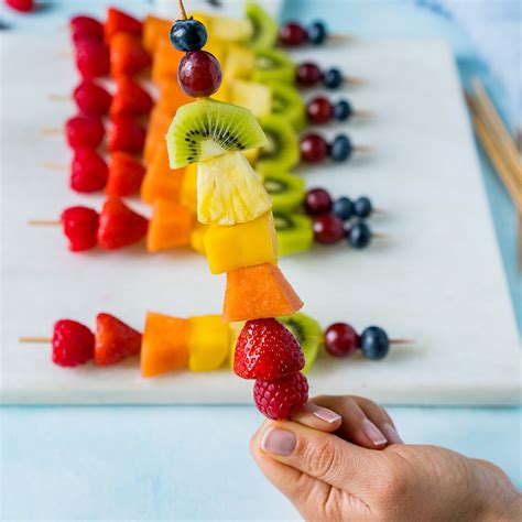 A Person Holding Up A Fruit Skewer With Berries And Kiwi On It