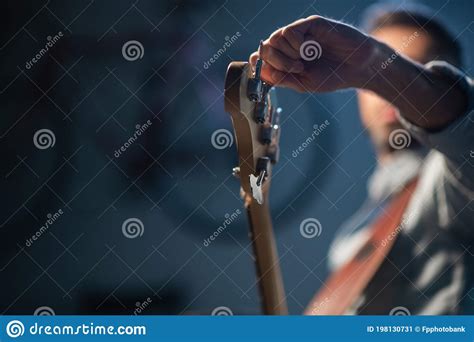 The Bassist Adjusts The Electric Bass Guitar In The Foreground Of The Pegs And Fretboard Close