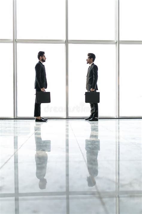 Two Businessmen Deep In Discussion Together While Standing In An Office