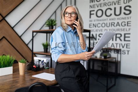 五十岁的女商人手里拿着文件在现代办公室里用手机说话高清摄影大图 千库网