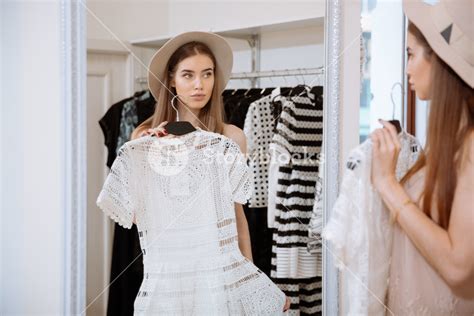 Attractive Young Woman Trying On Dress In Front Of Mirror In Clothing