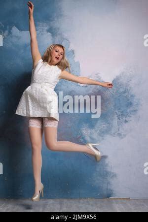 Long Legged Blonde Photomodel In White Minidress And White Stockings Posing At The Studio