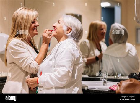 Side View Of Cheerful Mature Woman Applying Red Lipstick On Lips Of Smiling Aged Female Near