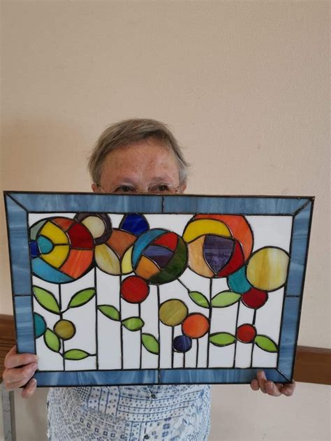 A Woman Is Holding Up A Stained Glass Panel With Flowers On It And Leaves In The Center