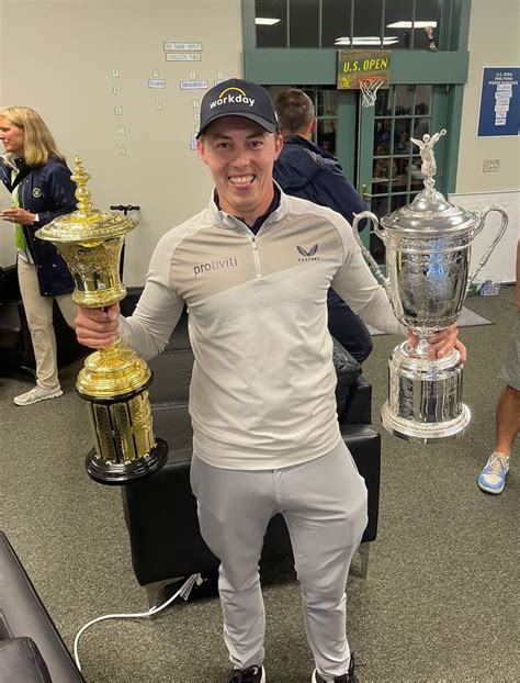 a man is holding two trophies and posing for the camera in front of other people