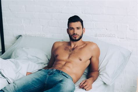 Handsome Muscular Shirtless Man In Jeans Posing On Bed At Home Stock