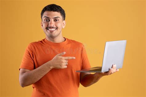 Happy Latin Man Pointing At Laptop Screen And Smiling Standing With Pc