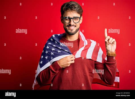 Young man wearing glasses and United States of America flag over isolated red background ...