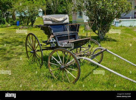 Old horse-drawn wooden buggy sits in the front yard of a house in a ...