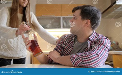 Angry Teenage Girl Taking Away Bottle Of Alcohol From Her Drunk Father Drinking On Kitchen