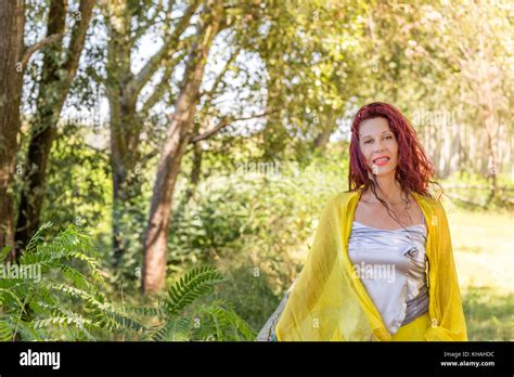 Portrait Of German Mature Woman With Yellow Shawl And Silver Top Smiling In A Green Garden Stock