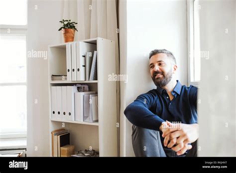 Mature Hipster Businessman Sitting On A Window Sill In A Modern Office
