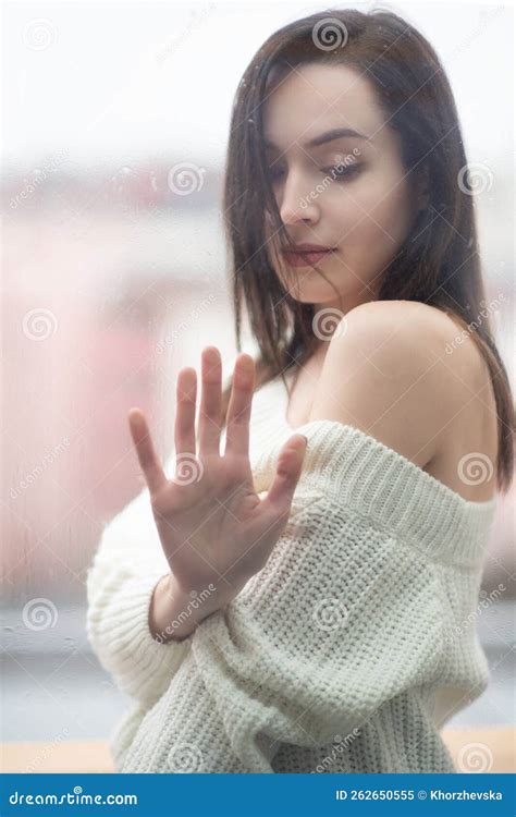 Young Beautiful Woman With Long Dark Hair Dressed In A White Sweater Outdoor Behind Window Pane