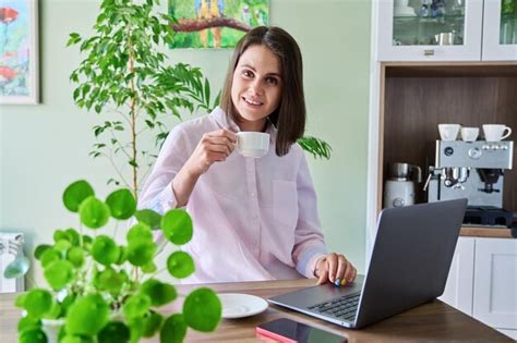 Premium Photo | Young woman sitting at home using laptop drinking ...