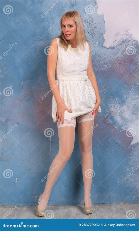 Long Legged Blonde Girl In Whi Minidress And White Stockings Posing At The Wall Stock Photo