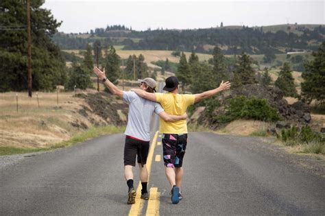 Two Men Walking Along Road Together Arms Raised Appreciating View