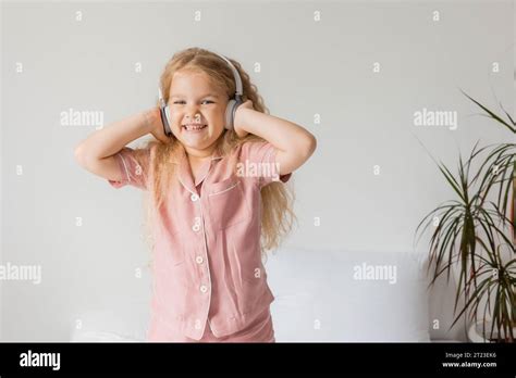 Cute Smiling Curly Haired Blonde Girl In Headphones Jumps In Bed Stock