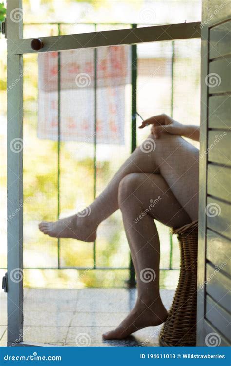 A Mosquito Net On The Balcony Door And Legs Of A Woman Sitting In The