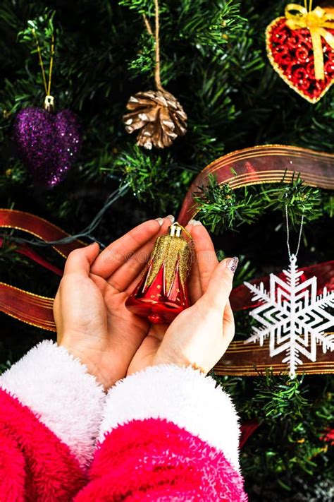 Hands Holding Christmas Ornament In Front Of Christmas Tree Decorating