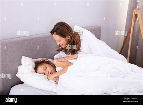 Mature Woman Waking Up Her Daughter Sleeping On Bed In Bedroom Stock