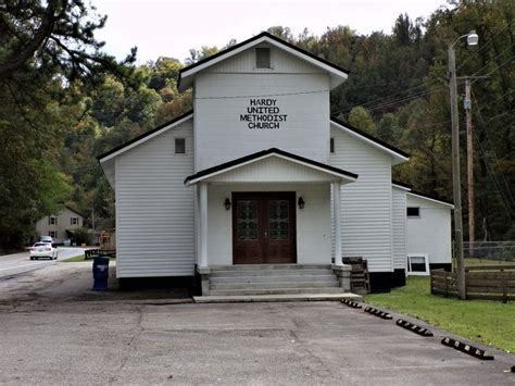 An Old White Church Sitting On The Side Of A Road In Front Of Some Trees