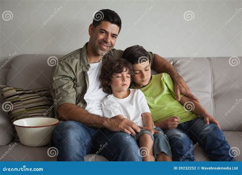 Father And Sleepy Sons With Popcorn Bowl Watching Tv In Living Room