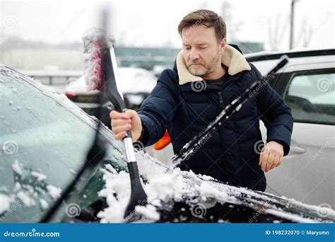 A Mature Man Cleans His Car With A Brush After A Snowfall Snowdrift