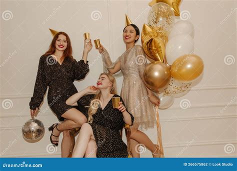 Happy Young Interracial Girls In Sparkly Dresses At Bachelorette Party Raise Paper Cups Indoors