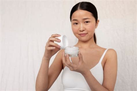 Mujer Coreana De Tiro Medio Posando Con Crema Para La Cara Foto Gratis