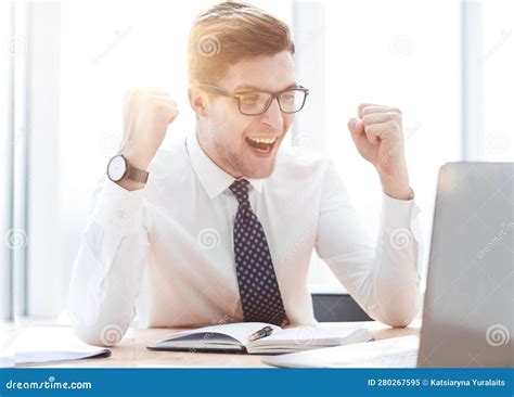 Happy Young Businessman Raising Hands In Front Of Laptop At Office Desk