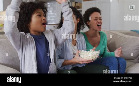 Mixed Race Lesbian Couple And Daughter Watching Tv Eating Popcorn High